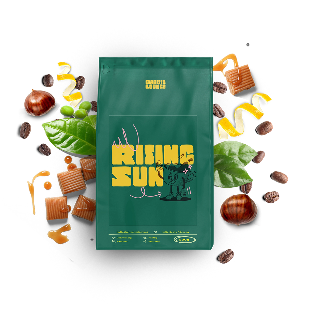 Barista Lounge Kaffeemischung 'Rising Sun' in grüner Verpackung, umgeben von Karamellwürfeln, Kaffeebohnen, Maronen und grünen Blättern. Die Verpackung zeigt ein gelbes Logo 'Rising Sun' mit einem fröhlichen Cartoon-Maskottchen. Diese Kaffeemischung zeichnet sich durch vollmundige, karamellige und nussige Aromen aus.